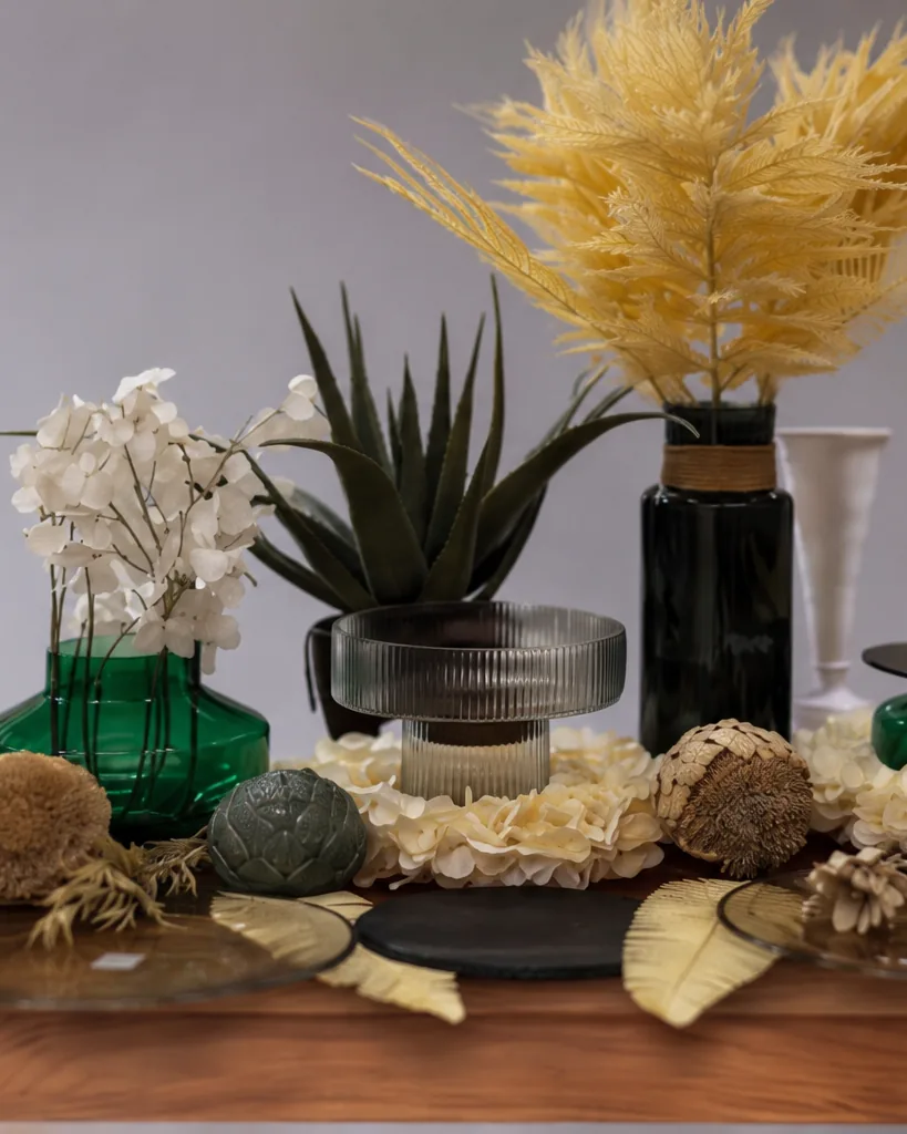 Nahaufnahme: Pampasgras über smaragdgrünem Glas, davor Trockenblüten und Aloe.