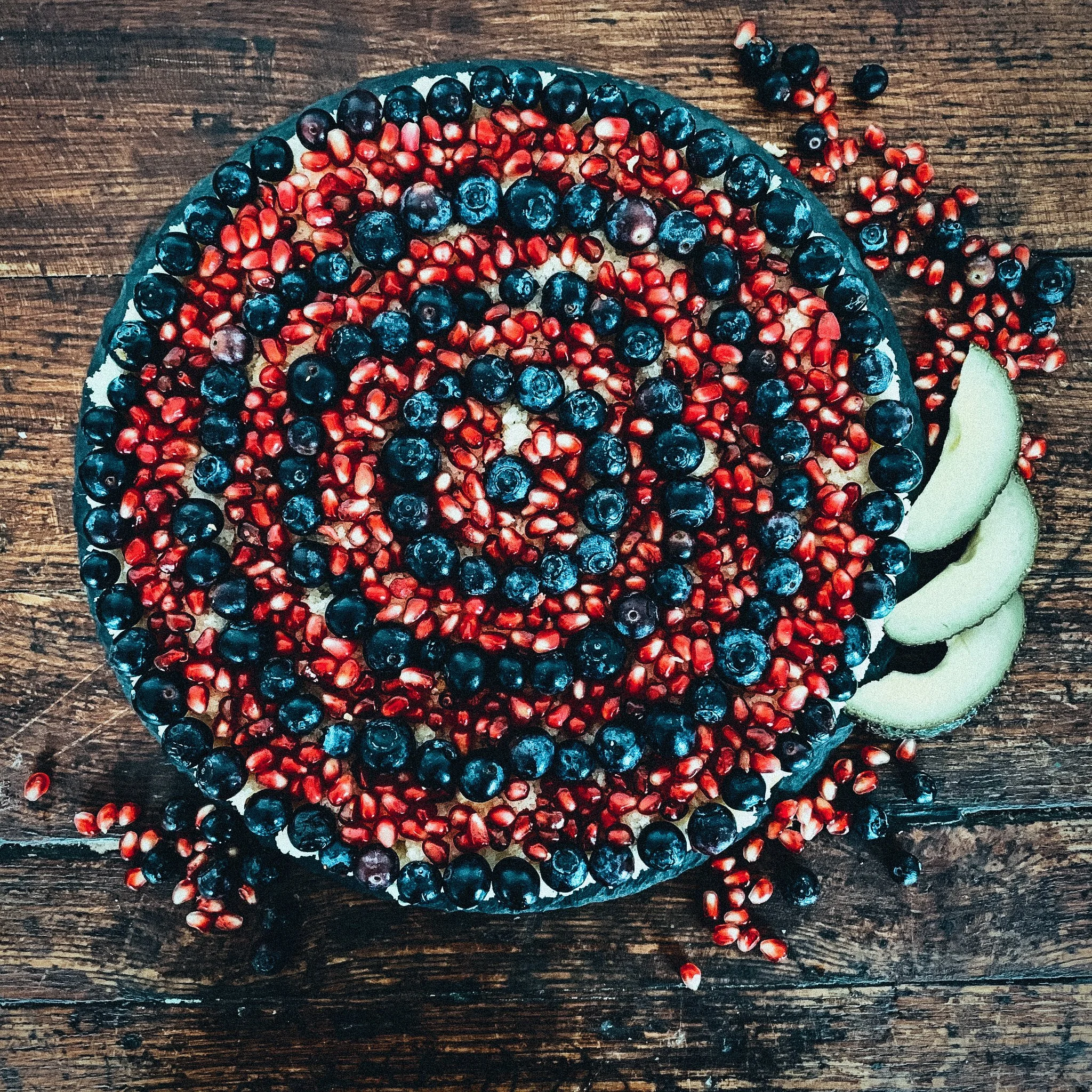 Fruchttorte mit Blaubeeren, Granatapfelkernen und Avocadoscheiben auf einem Holztisch.