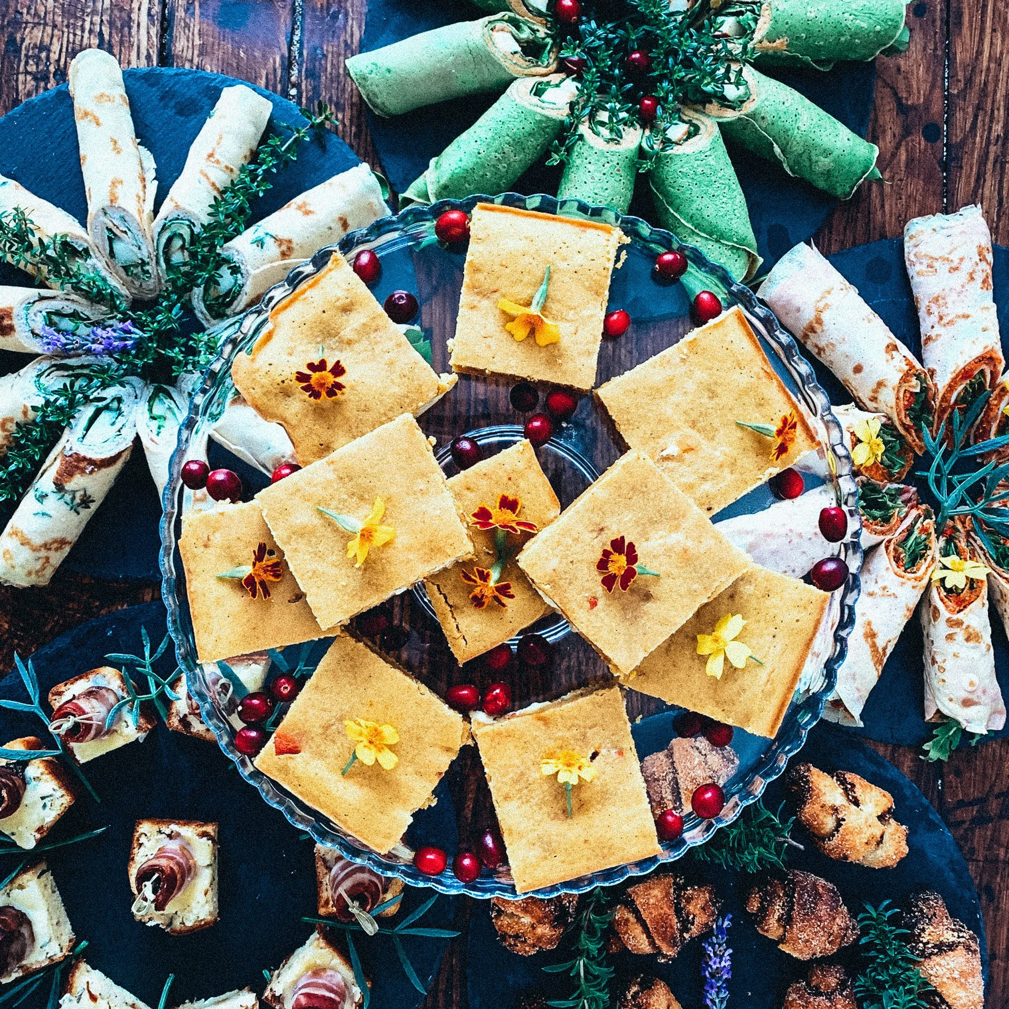 Verschiedene Arten von Gebäck und Wraps auf einem Tisch, dekoriert mit essbaren Blüten und Kräutern, auf Servierplatten angerichtet.