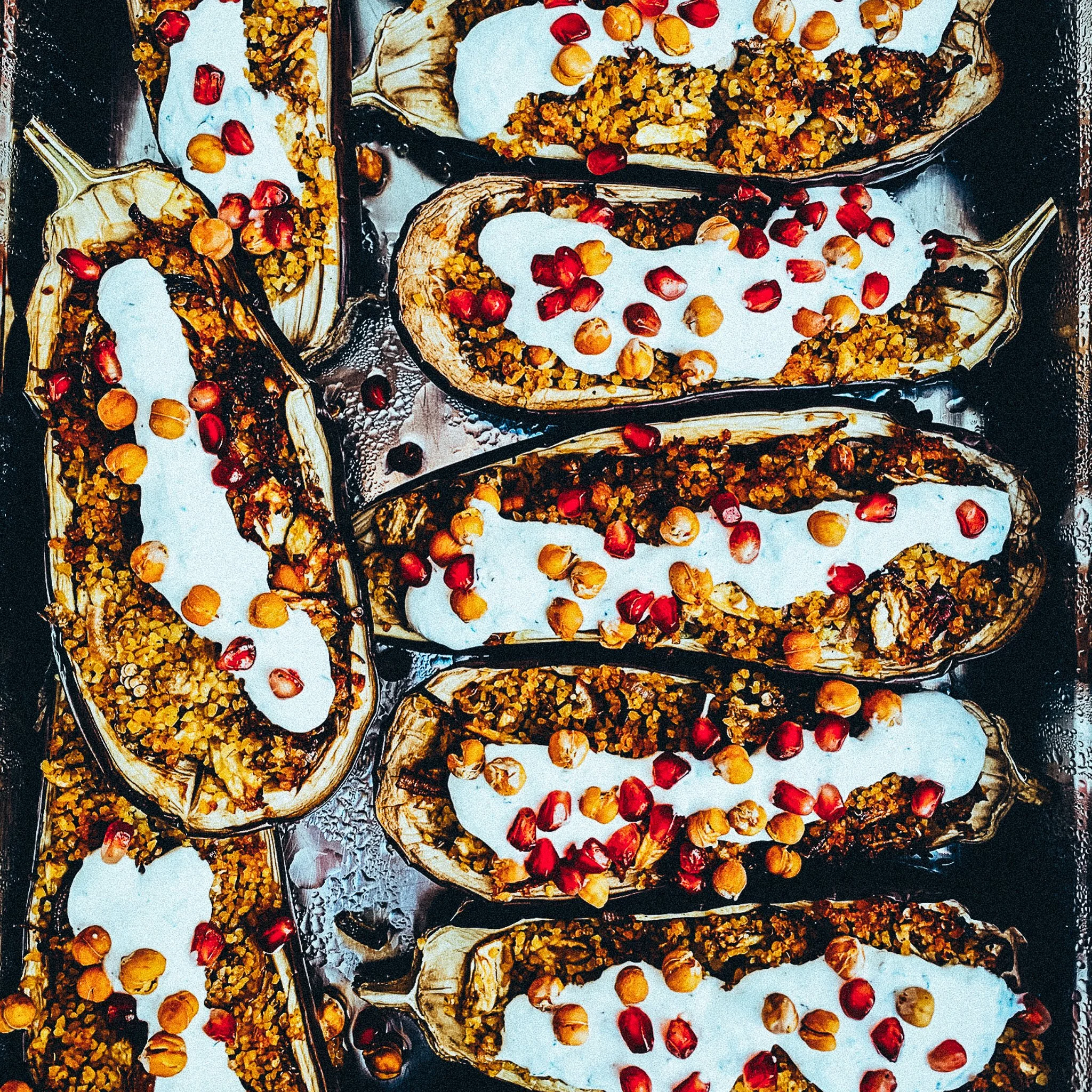 Gefüllte Auberginenhälften mit Joghurt, Kichererbsen und Granatapfelkernen auf einem Backblech.