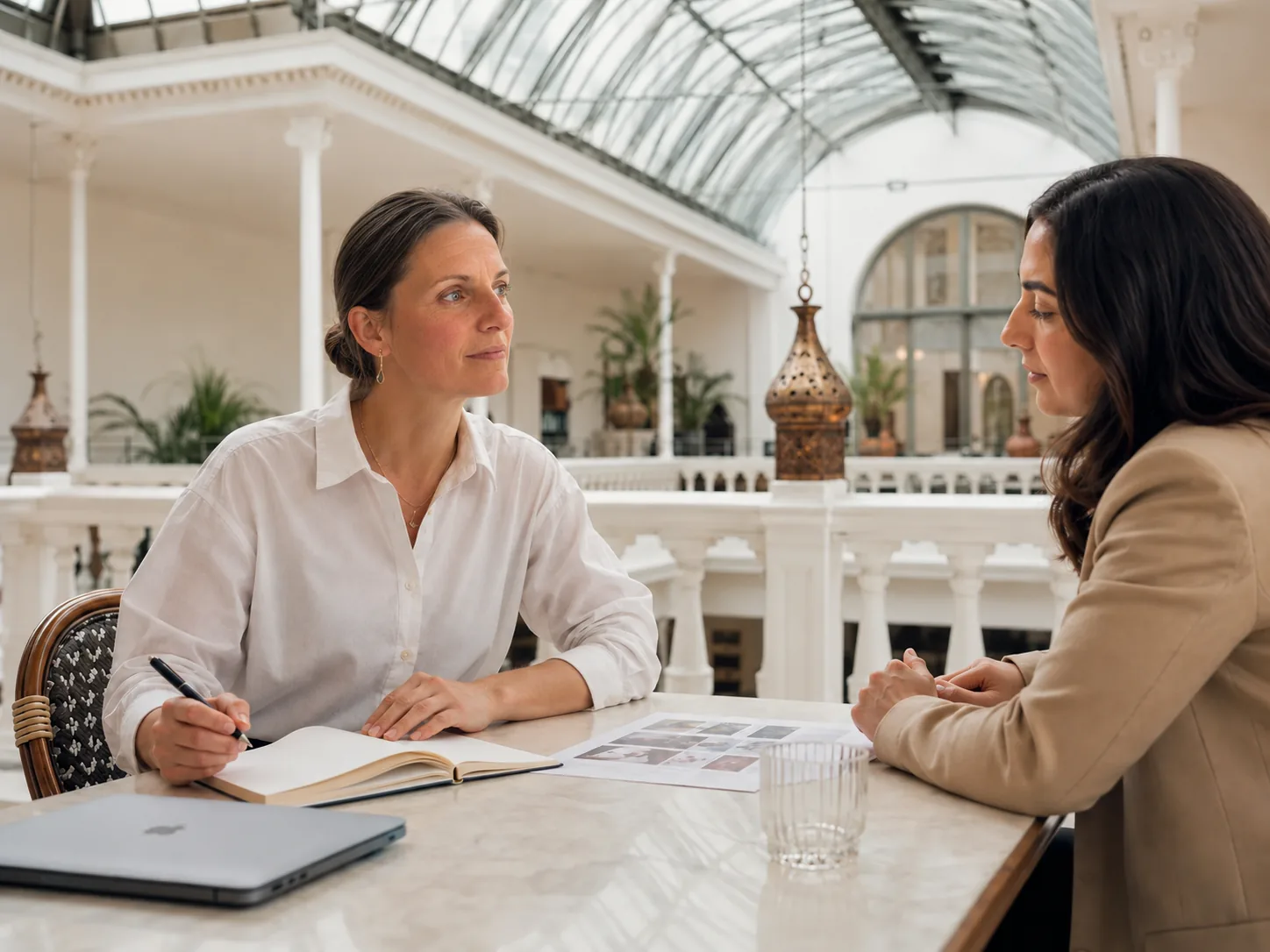 Zwei Frauen besprechen an einem Tisch ein Angebot, daneben Notizbuch und Bildvorlagen