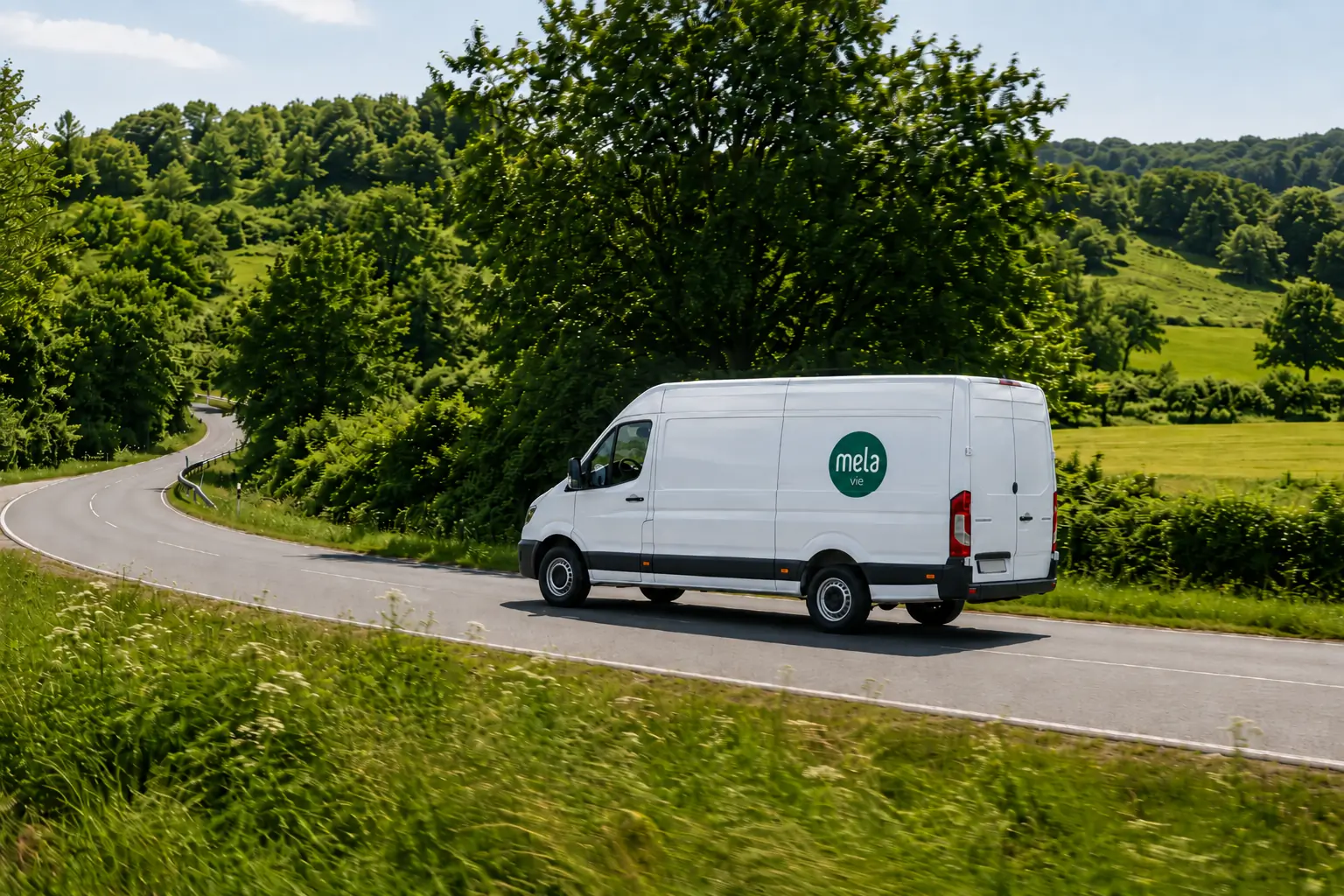 Weißer Transporter mit dem Zeichen von Melavie auf einer Landstraße zwischen bewaldeten Hügeln
