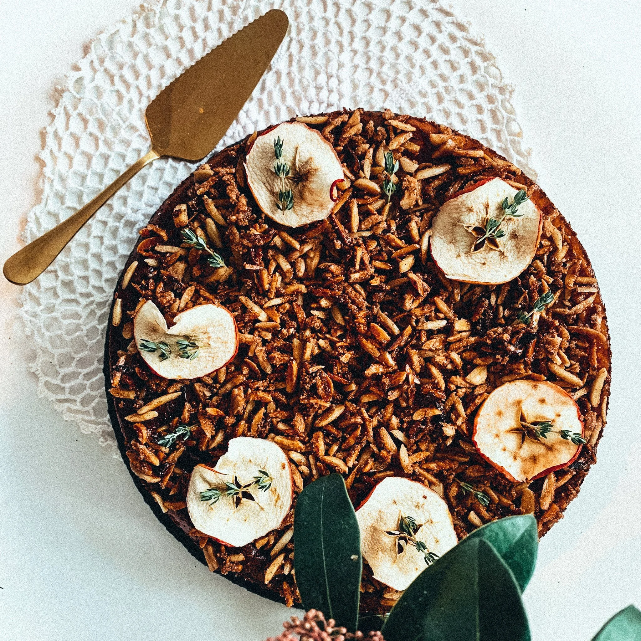 Obstkuchen mit Mandeln und Apfelscheiben dekoriert auf weißem Tischtuch, daneben goldene Tortenheber.
