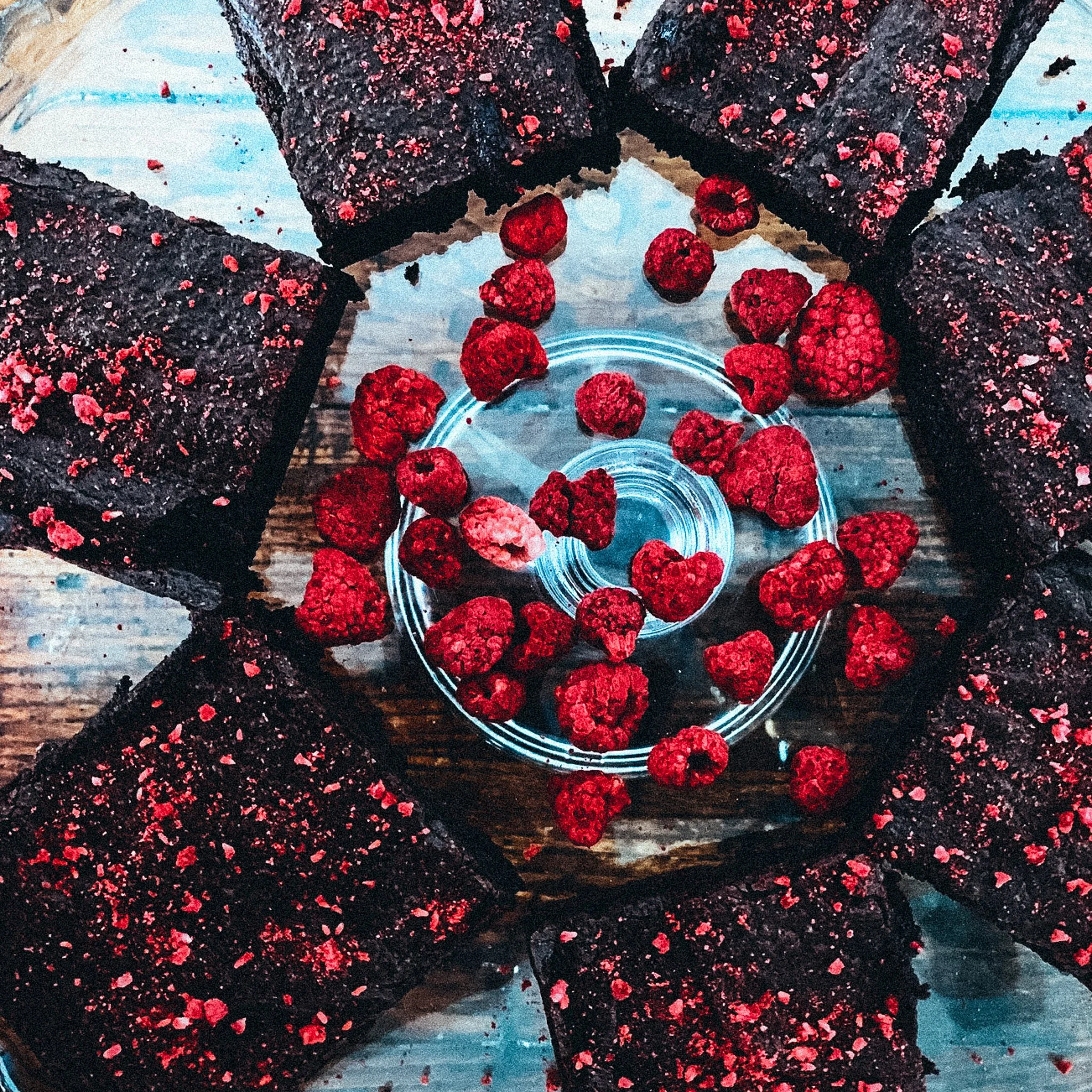 Schokoladenkuchenstücke mit Himbeeren auf einem Holztisch arrangiert, in einer kreisförmigen Anordnung.